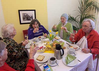 5 Bewohnerinnen an einem gedeckten Tisch beim Kaffee-Trinken und auf einen Geburtstag anstoßen